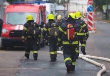 Firefighters walking toward a scene with hoses and a red emergency van