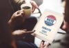 Hands holding a tablet with a voting screen and a person holding coffee