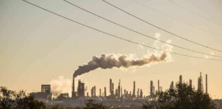 Industrial refinery with smokestack emitting plume at sunset