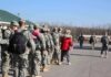 Soldiers in uniform line up outdoors with gear