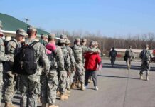Soldiers in uniform line up outdoors with gear