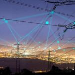 Power transmission towers over a city at dusk with connected network lines