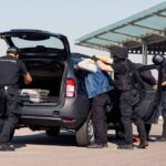 customs officers detain a person beside a car with its trunk open