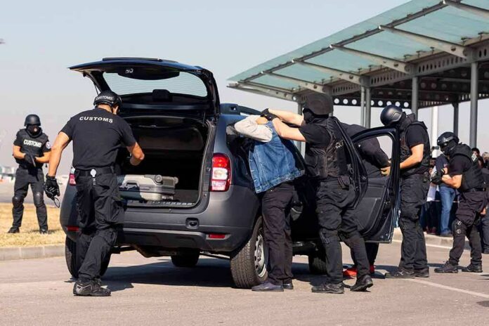 shutterstock_1428097139-1 customs officers detain a person beside a car with its trunk open