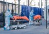 Healthcare workers in PPE move covered stretchers outside a facility