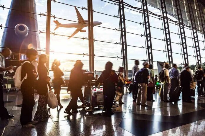 Passengers queue inside an airport terminal at sunset